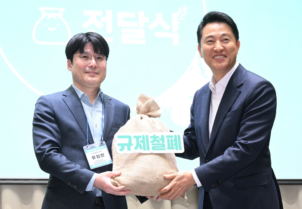 사진2. 오세훈 서울시장이 7일(수) 열린 「규제철폐 100일 성과보고회」에서 시민 제안이 담긴 규제철폐 모래주머니를 전달받고 있다.