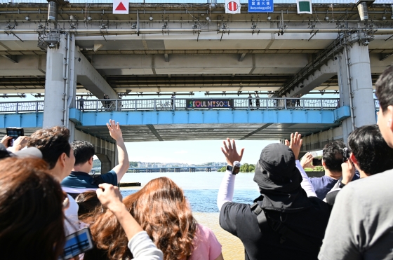 사진12. 주말 한강버스에 오른 시민들이 반포대교 아래를 지나며 다리 위 시민들과 손을 흔들며 즐거운 시간을 보내고 있다.